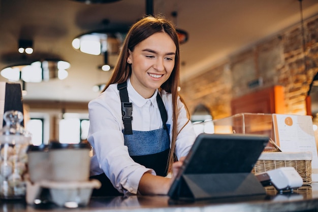 コーヒーショップで注文するタブレットを持つ女性のバリスタ