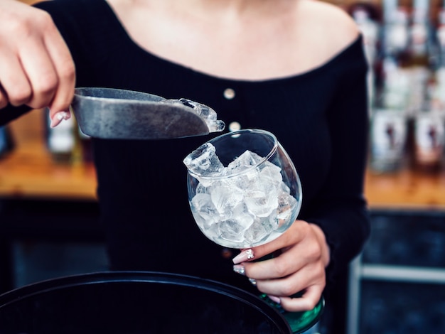 Free photo female bartender adding ice cubes to glass