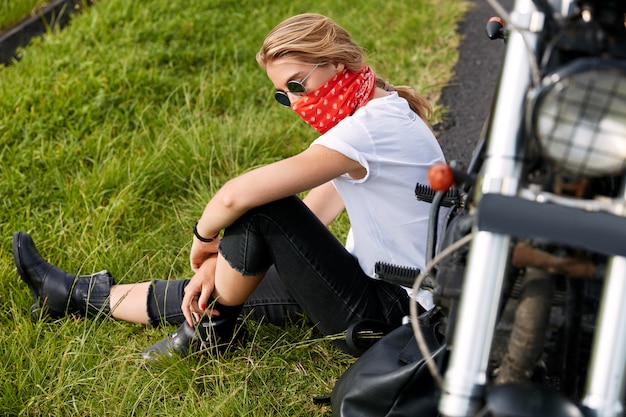 バイクの横にある草の上に座っている女性バイカー