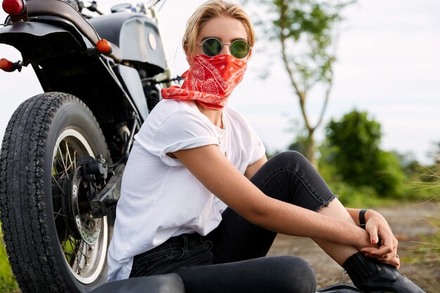 バイクの隣に座っている女性のバイカー