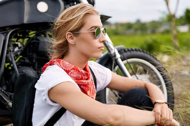 Female biker sitting next to motorbike