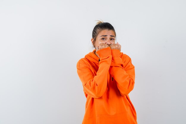 Female biting fists emotionally in orange hoodie and looking frightened 