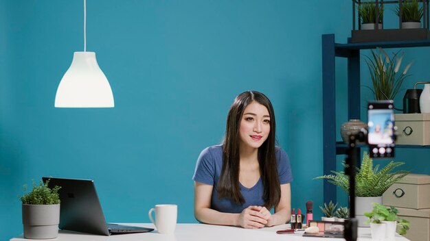 Female blogger recording makeup tutorial on camera in studio, talking about beauty products and glam cosmetics on social media vlog. Lifestyle influencer giving beauty tips on channel.