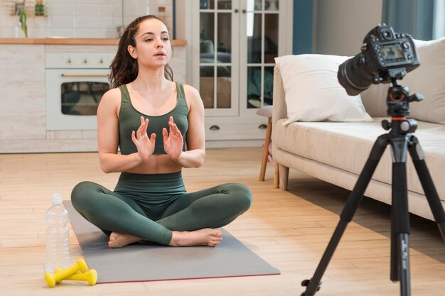 Женский блоггер в спортивной одежде, сидя на коврик для йоги