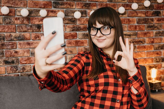 female blogger streaming online with smartphone and giving okay sign