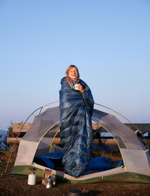 Foto gratuita femmina bionda che riposa in tenda avvolta nel sacco a pelo all'aperto