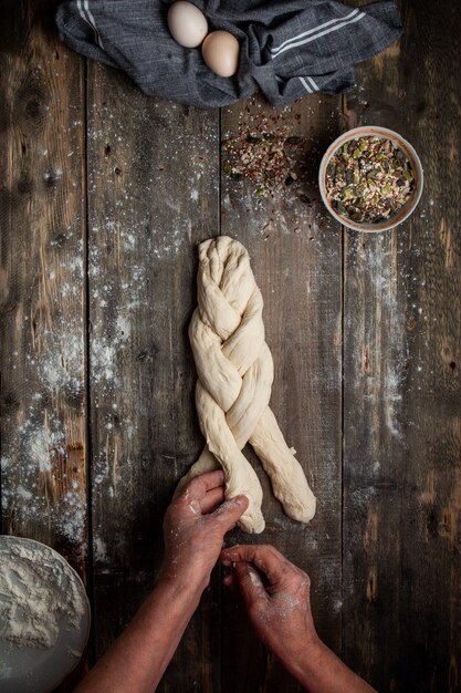 Female braiding dough with hands on wooden table top view