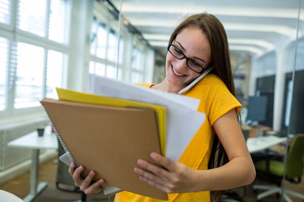 Female business executive holding a file and talking on mobile phone