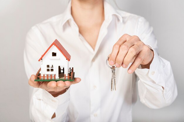 Женщина в деловом костюме держит игрушку модель дома и ключи