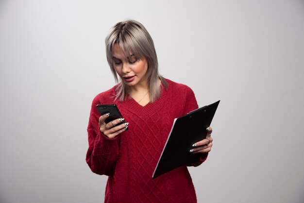 Female businesswoman looking at her cellphone on gray background.