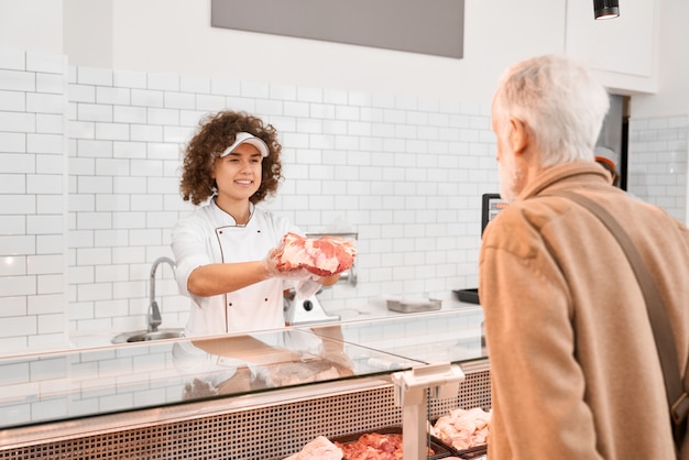 Foto gratuita macellaio femmina che dimostra carne all'uomo anziano.