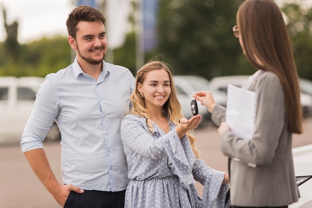 Female car dealer offering keys to a couple