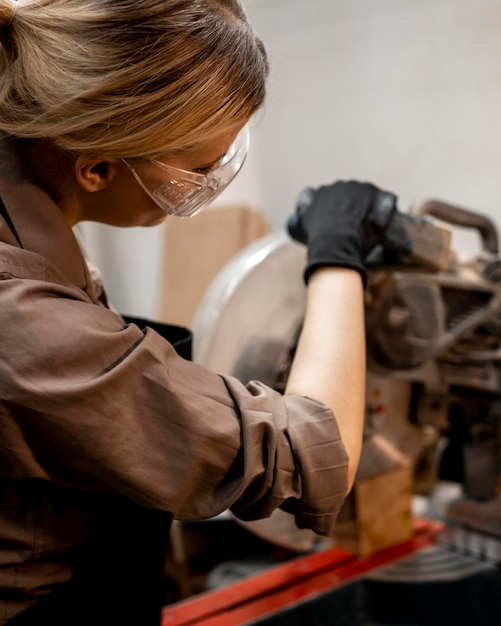 Female carpenter with glasses using electric saw