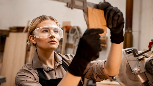 Female carpenter with glasses using tool to measure wood