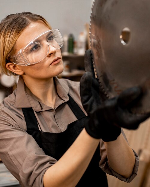 Female carpenter with safety glasses checking saw blade