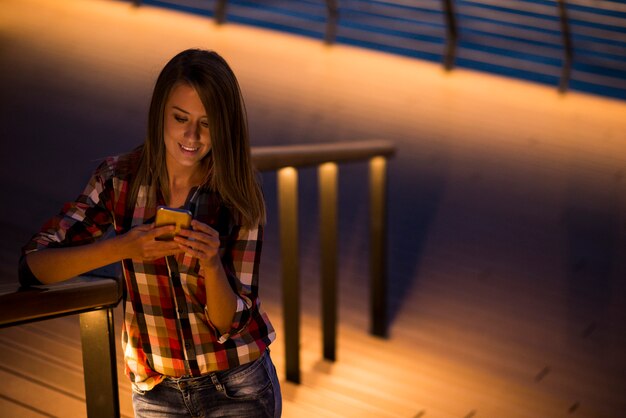 female caucasian student reading text messages on cell phone with reflected on her face screen light, blank screen phone