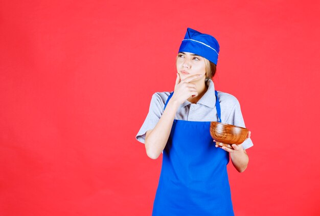 Female chef in blue apron holding a chinese copper noodle cup and thinking