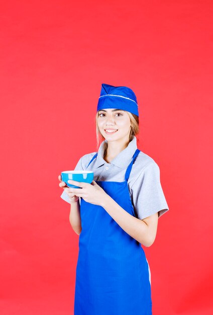Female chef in blue apron holding a noodle cup