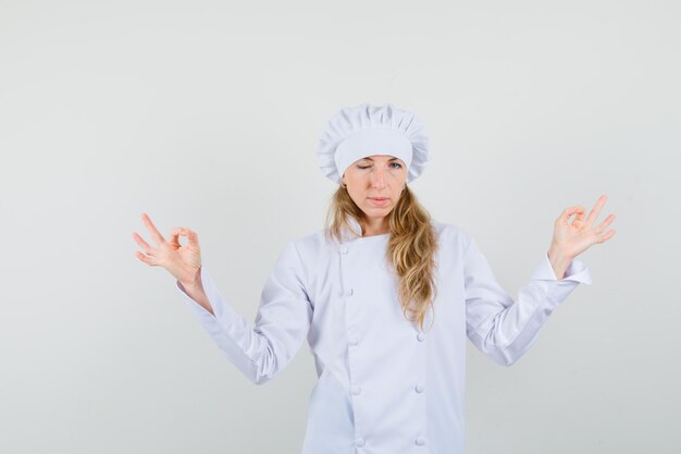 Female chef doing meditation and winking eye in white uniform 