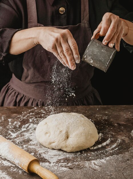 피자 반죽 위에 밀가루를 뿌리는 여성 요리사