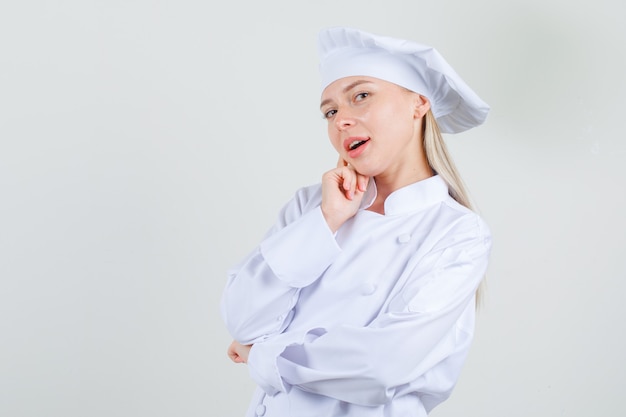 무료 사진 여성 요리사 흰색 유니폼에 뺨에 손가락을 잡고 매력적인 찾고.
