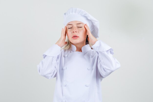 Female chef holding fingers on temples in white uniform and looking tired 