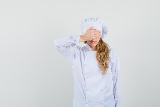 Female chef holding hand on eyes in white uniform and looking frightened 