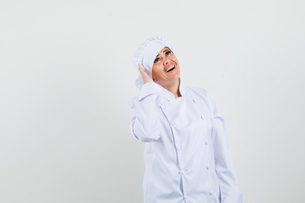 Женщина-шеф-повар держит руку возле уха в белой форме и выглядит весело