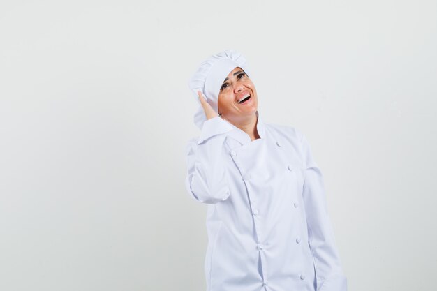 Female chef holding hand near ear in white uniform and looking merry