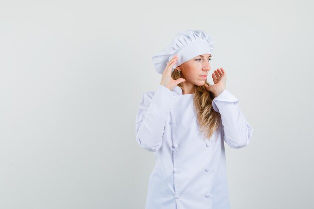 Female chef holding hands near face and looking aside in white uniform 