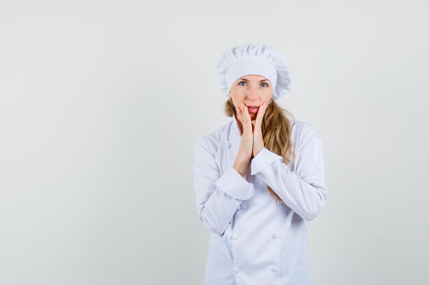 Female chef holding hands near mouth in white uniform and looking elegant 