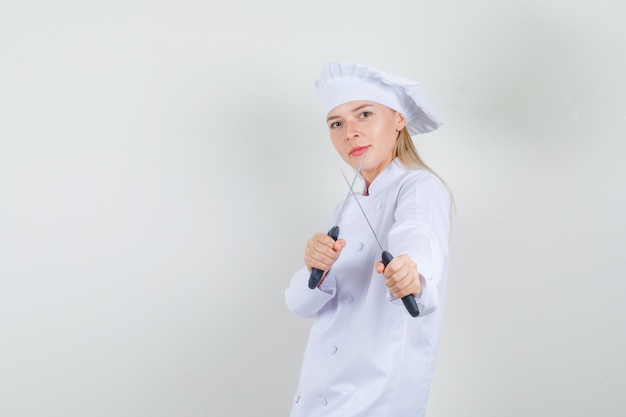 Female chef holding knives in boxer pose in white uniform