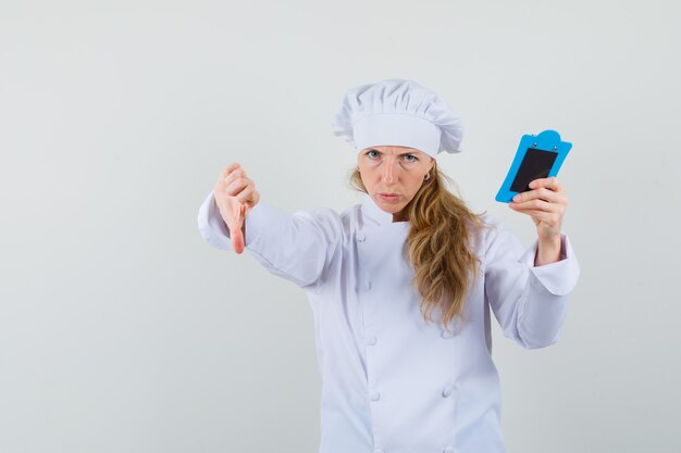 Female chef holding mini clipboard with thumb down in white uniform 
