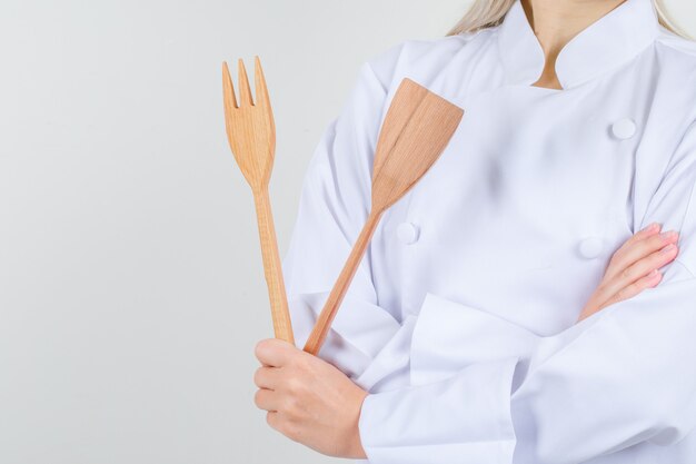 Female chef holding wooden fork and spatula in white uniform 