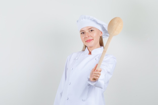 Female chef holding wooden spoon in white uniform and looking cheery.