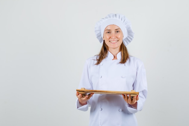 Female chef holding wooden tray in white uniform and looking cheerful. front view.