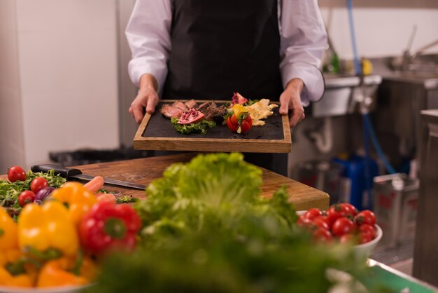 야채 장식으로 구운 쇠고기 스테이크 접시를 들고 호텔 또는 레스토랑 주방의 여성 요리사
