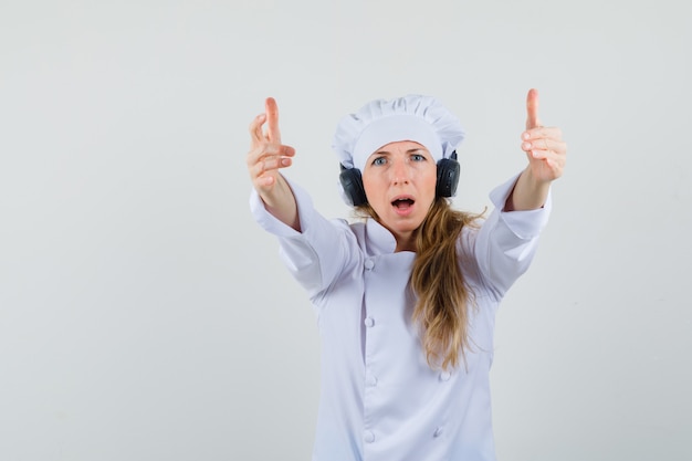 Female chef inviting to come while wearing headphones in white uniform 