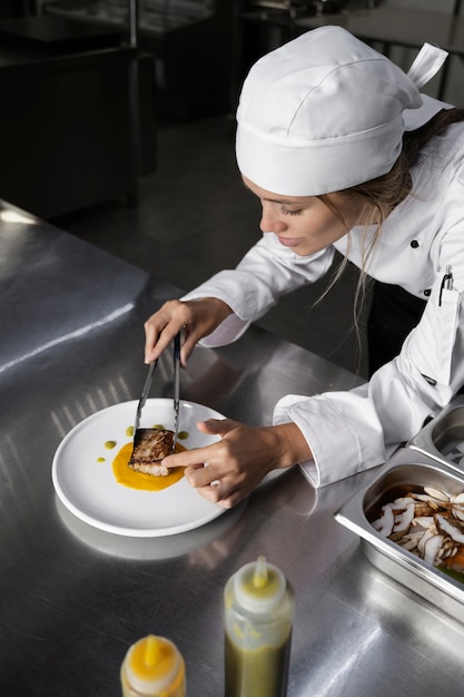 Foto gratuita cuoco unico femminile in cucina che prepara piatto di bistecca