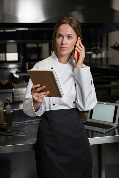 Female chef in the kitchen talking on the phone and using notebook