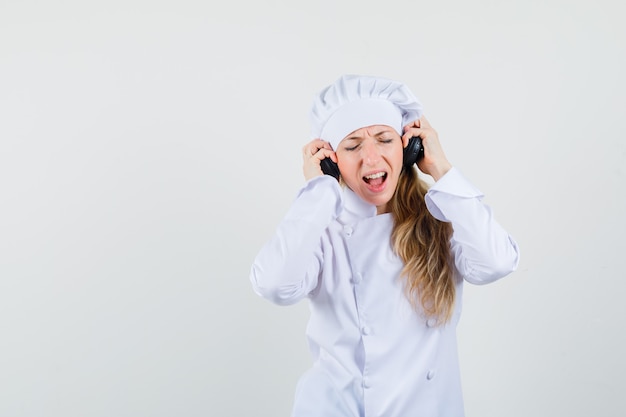 Cuoco unico femminile che ascolta la musica con le cuffie in uniforme bianca e sembra felice