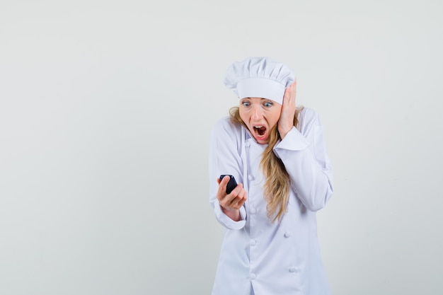 Female chef looking at cellphone in white uniform and looking shocked. 