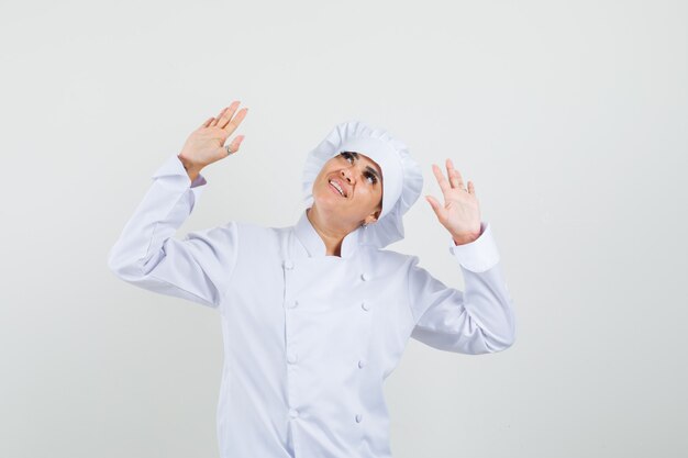 Female chef looking up, raising palms in white uniform and looking cheerful. 