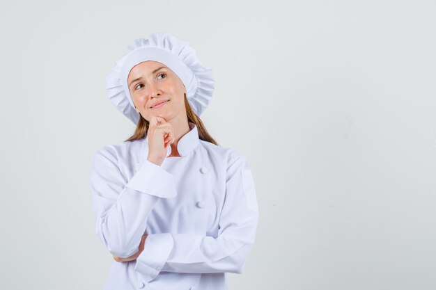 Foto gratuita cuoco unico femminile che osserva in su con la mano sul mento in uniforme bianca e che sembra promettente. vista frontale.