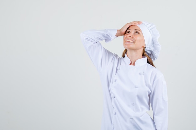 Foto gratuita cuoco unico femminile che osserva in su con la mano sulla testa in uniforme bianca e che sembra contento. vista frontale.