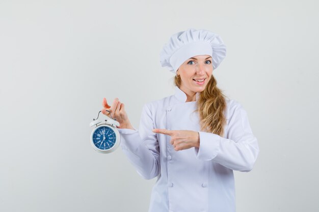 Женщина-шеф-повар указывает на будильник в белой форме и выглядит весело