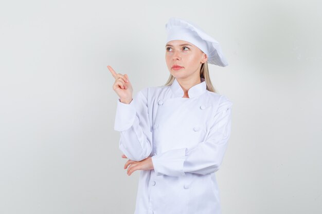 Female chef pointing away and looking aside in white uniform 