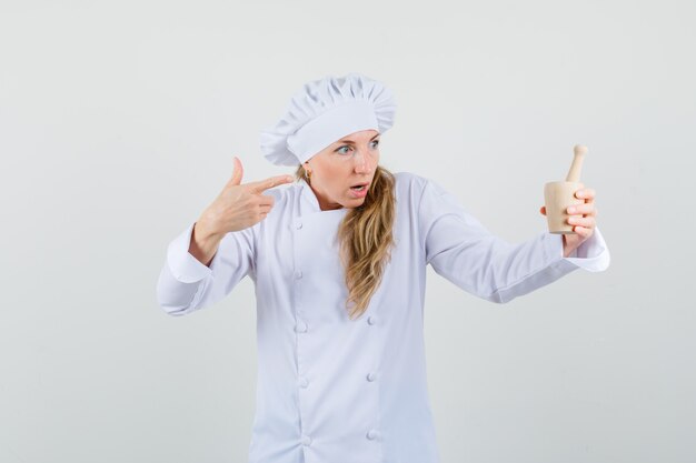 Female chef pointing at mortar with pestle in white uniform and looking surprised. 