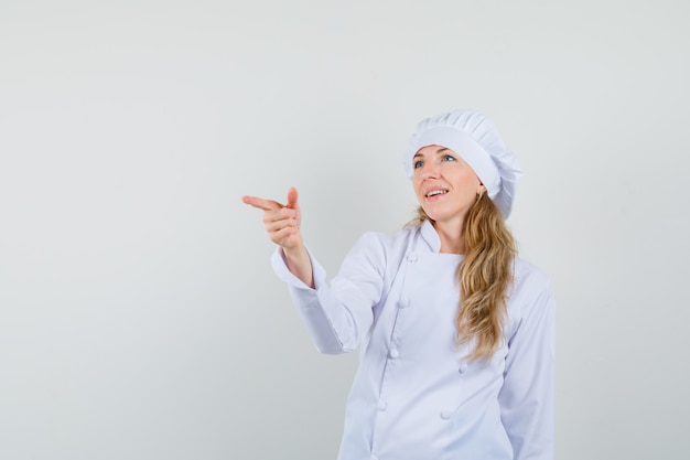 Cuoco unico femminile che indica al lato in uniforme bianca e che sembra allegro.