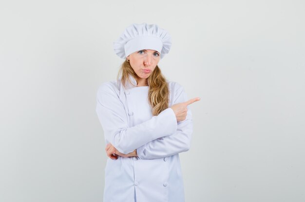 Female chef pointing to the side in white uniform and looking offended. 